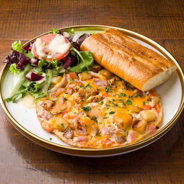 A L'ORANGE CAFE omelet with melted cheese, potatoes, ham, salad, and a baguette on a white plate.