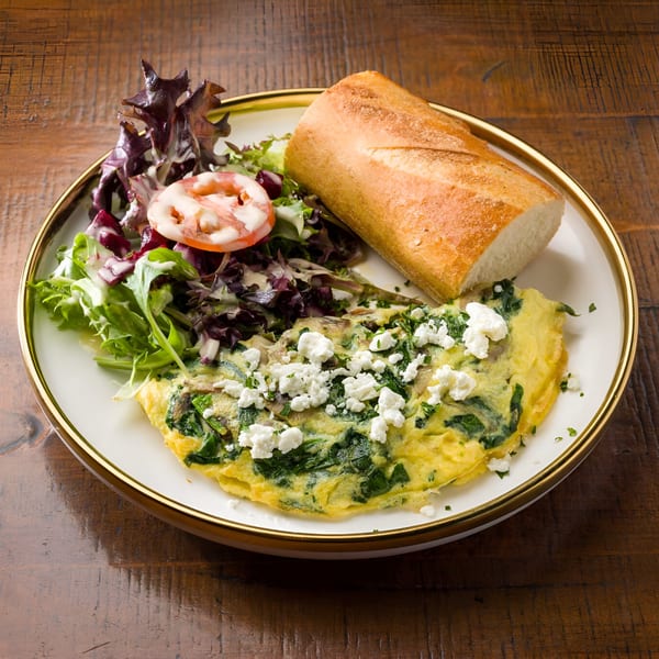 A spinach and feta omelet with a side salad and baguette on a white plate.