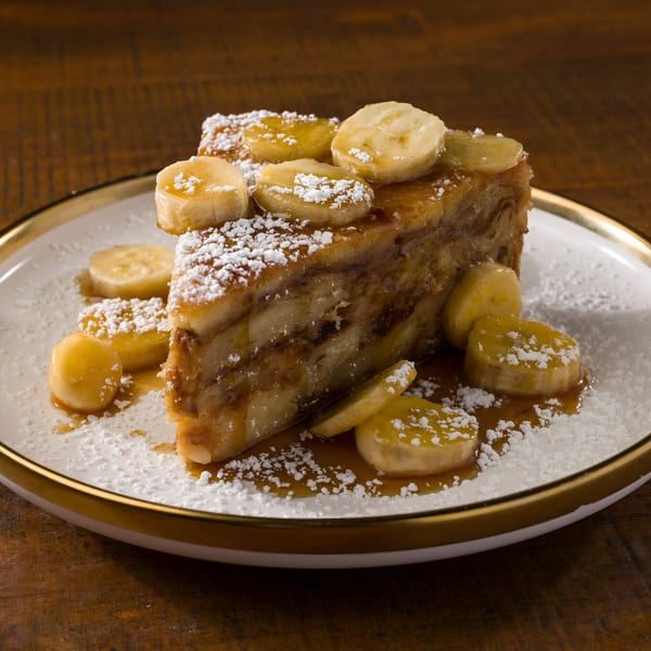 A slice of banana bread pudding with powdered sugar and caramel sauce on a white plate.