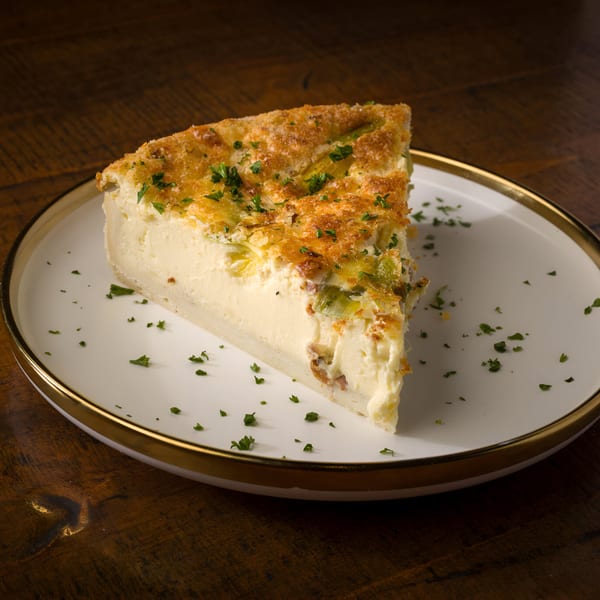 A slice of L'ORANGE CAFE's quiche with a golden crust and parsley on a white plate.